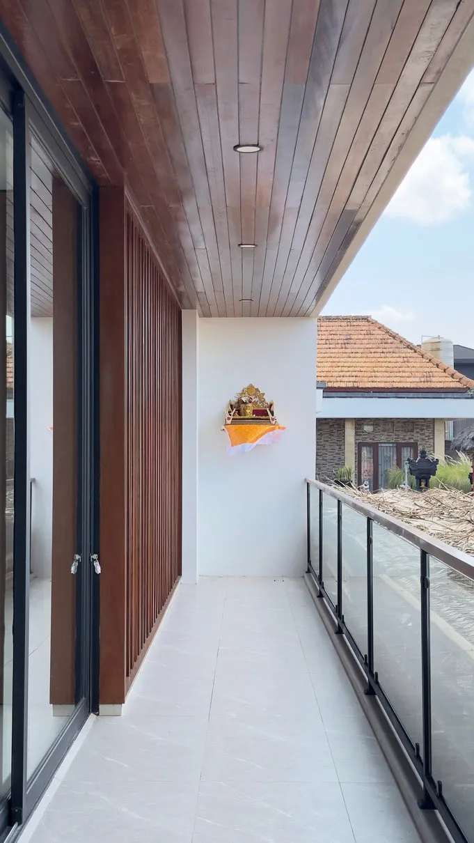 Balkon dengan langit-langit kayu, pagar kaca, dan pintu geser kaca.