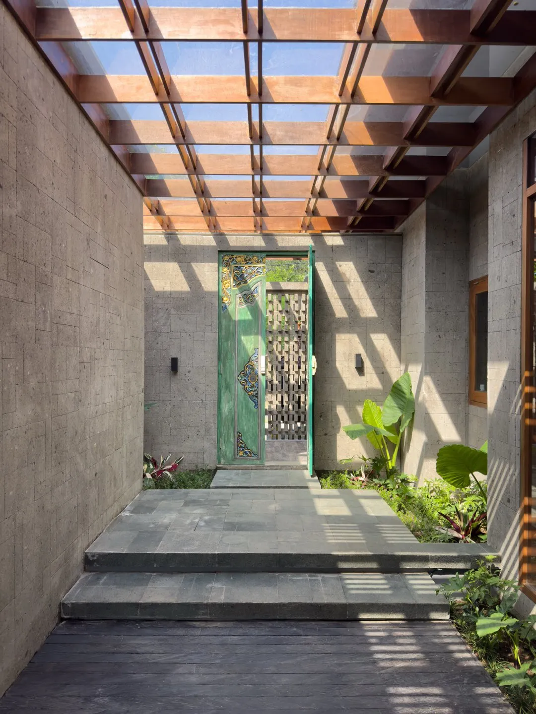 Koridor dengan dinding beton dan pergola kayu di atasnya.