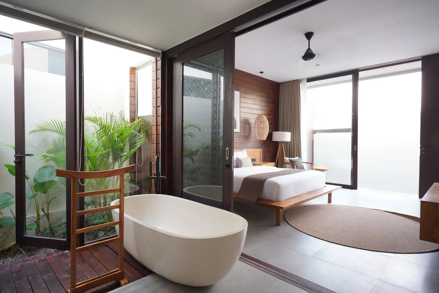 Kamar tidur dengan bathtub putih di dekat jendela kaca dan taman kecil.