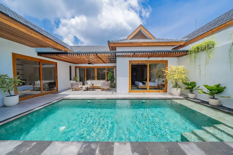 Kolam renang di depan villa beratap kayu pada siang hari.