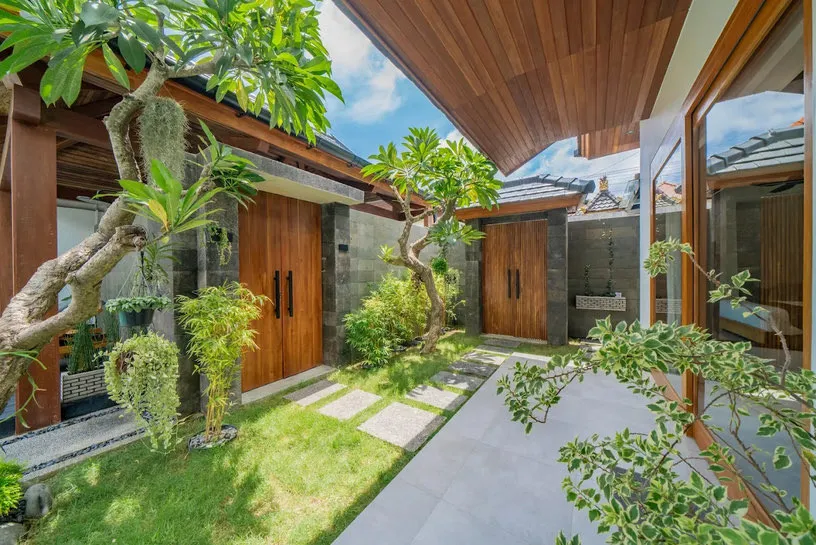 Taman dengan pohon kamboja dan pintu kayu menuju kamar.