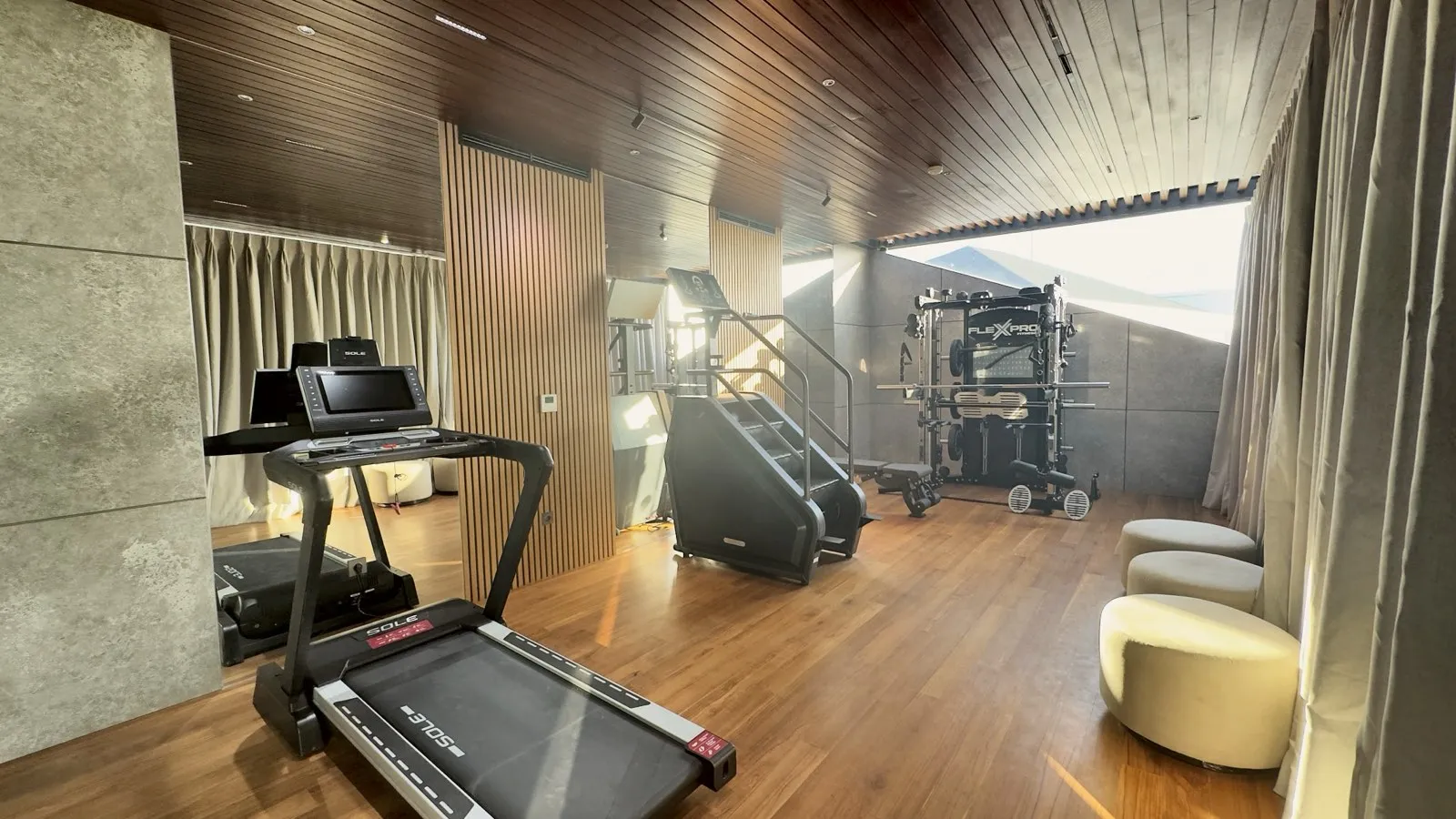 Ruang gym berlantai kayu dengan panel kisi kayu dan tirai.