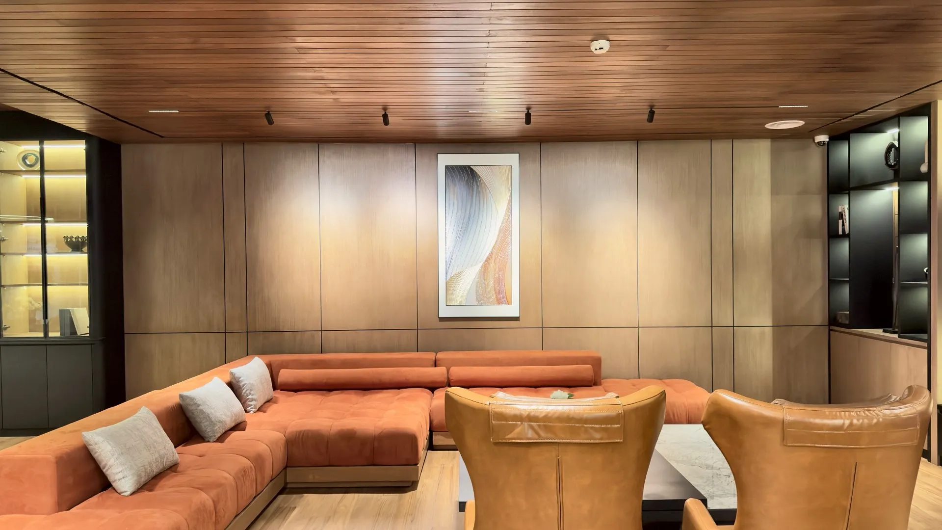 Ruang lounge dengan plafon dan panel dinding kayu, sofa oranye dan kursi kulit.