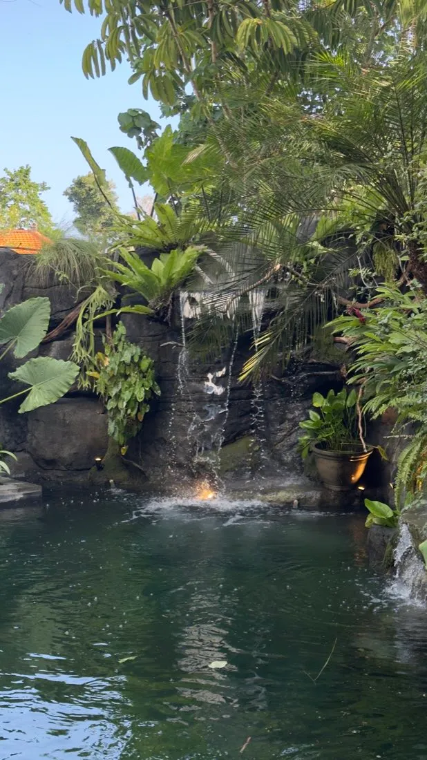 Kolam ikan dengan air terjun kecil dan taman tropis.