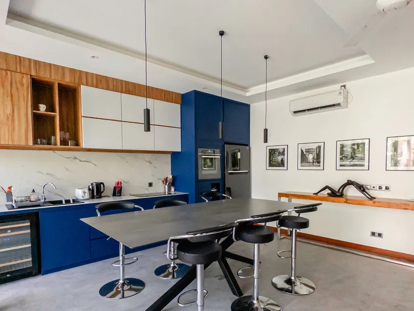 Dapur dengan lemari biru dan kayu serta meja panjang berkursi bar.