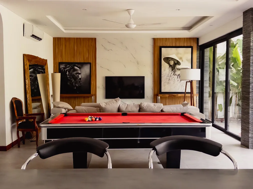 Ruang santai dengan meja biliar merah dan sofa di belakangnya.